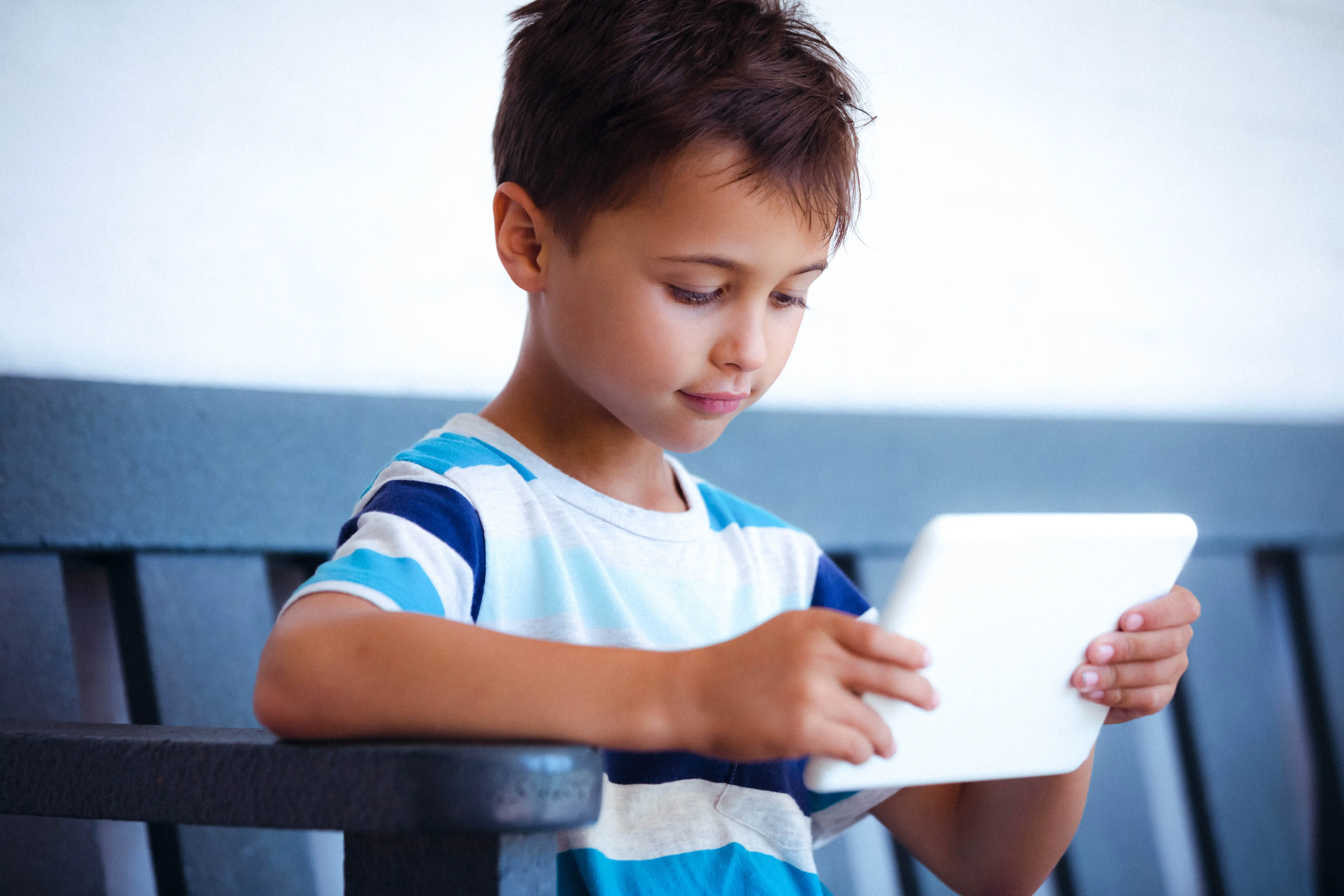 A boy using a digital tablet while sitting on a bench